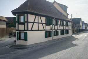 Façade à colombages rénovée d'une maison alsacienne à l'angle d'une rue, volets verts