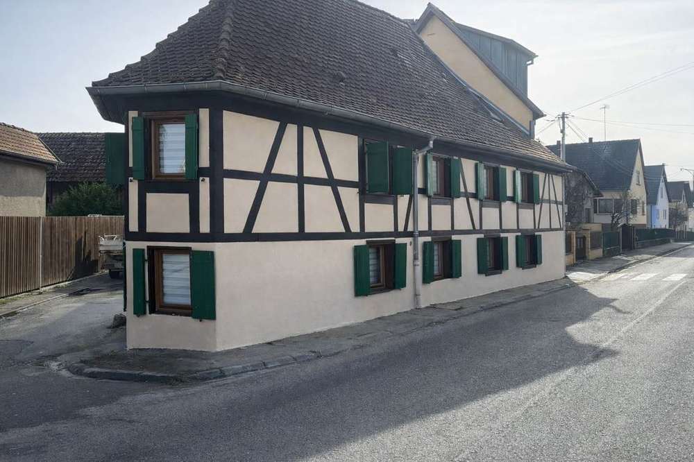 Façade à colombages rénovée d'une maison alsacienne à l'angle d'une rue, volets verts